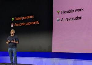 Image of Drew Houston, CEO of Dropbox standing on a stage in front of a screen with the words Global Pandemic and Economic Uncertainty on the left and the words Flexible work and AI revolution on the right.